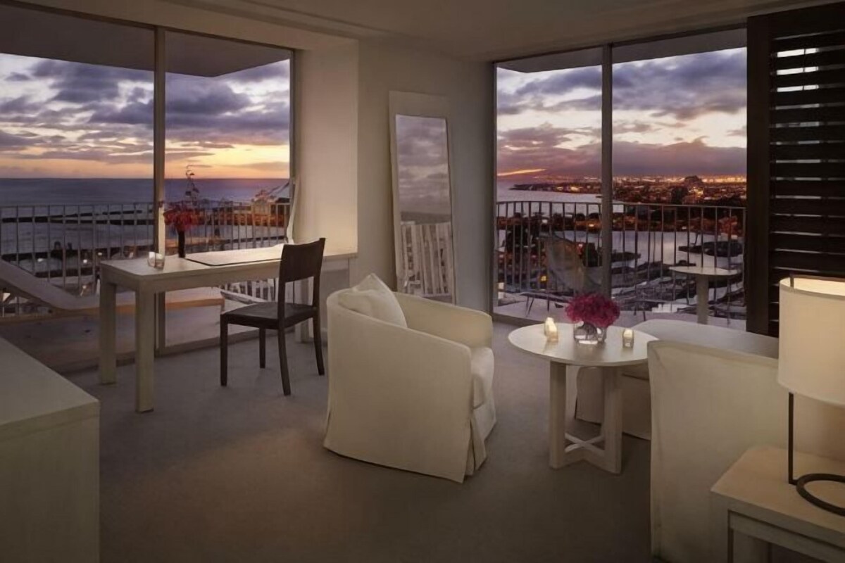 Une chambre d’hôtel moderne dotée d’un balcon, d’un coin repas et d’un espace salon offrant une vue sur la ville et la mer.