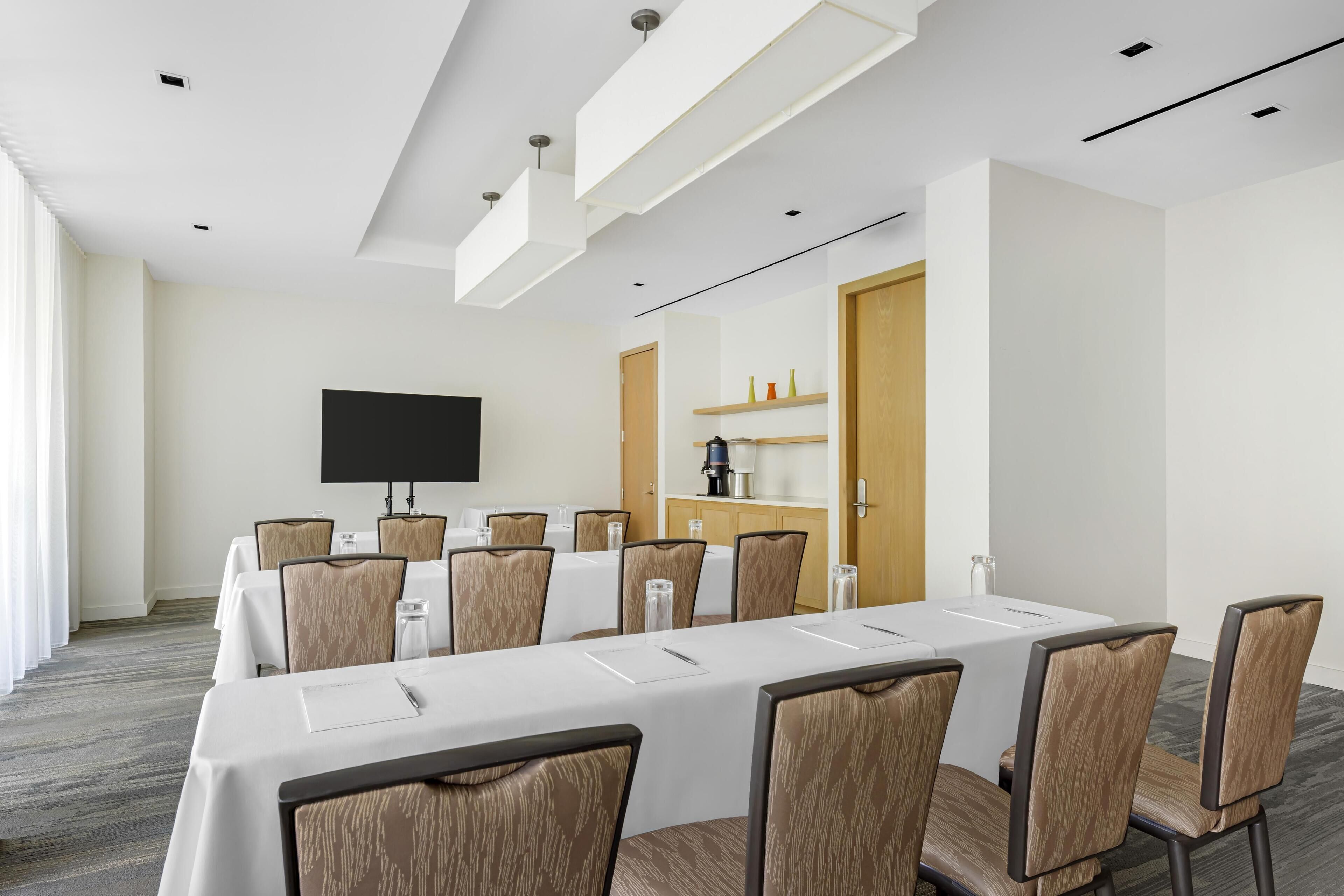 Una sala de conferencias con una larga mesa, sillas, un televisor de pantalla plana y una máquina de café.