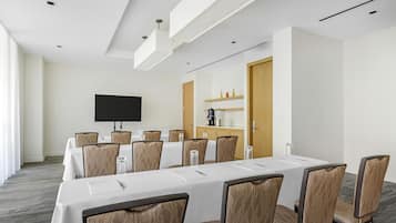 Una sala de conferencias con una larga mesa, sillas, un televisor de pantalla plana y una máquina de café.