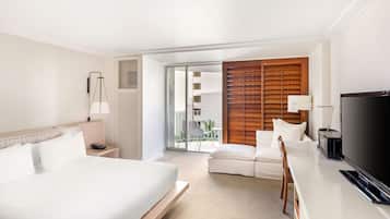 Une chambre d’hôtel comprenant un lit, un bureau avec une télévision, une chaise et une porte coulissante donnant sur un balcon.