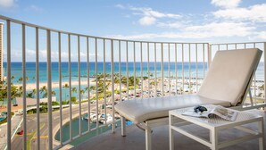 A balcony with a white cushioned chair, a small table with a newspaper and headphones, and a view of the beach and ocean. - Hilton Vacation Club The Modern Honolulu (Honolulu)