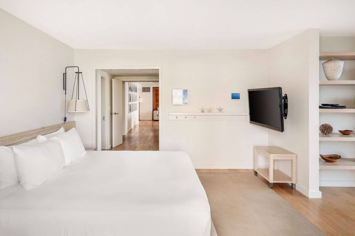 A hotel room with a bed, a TV, a small table, and a shelf with decorative items.