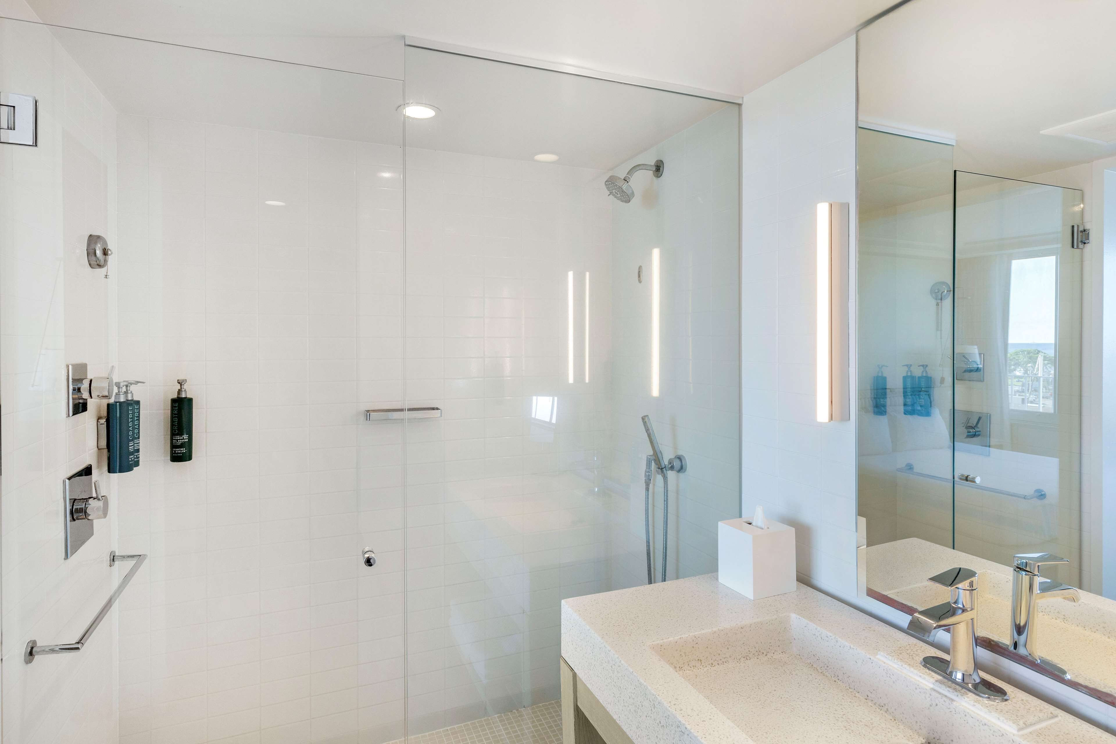 A modern bathroom with a glass-enclosed shower, a large mirror, and a countertop with a sink and faucet.
