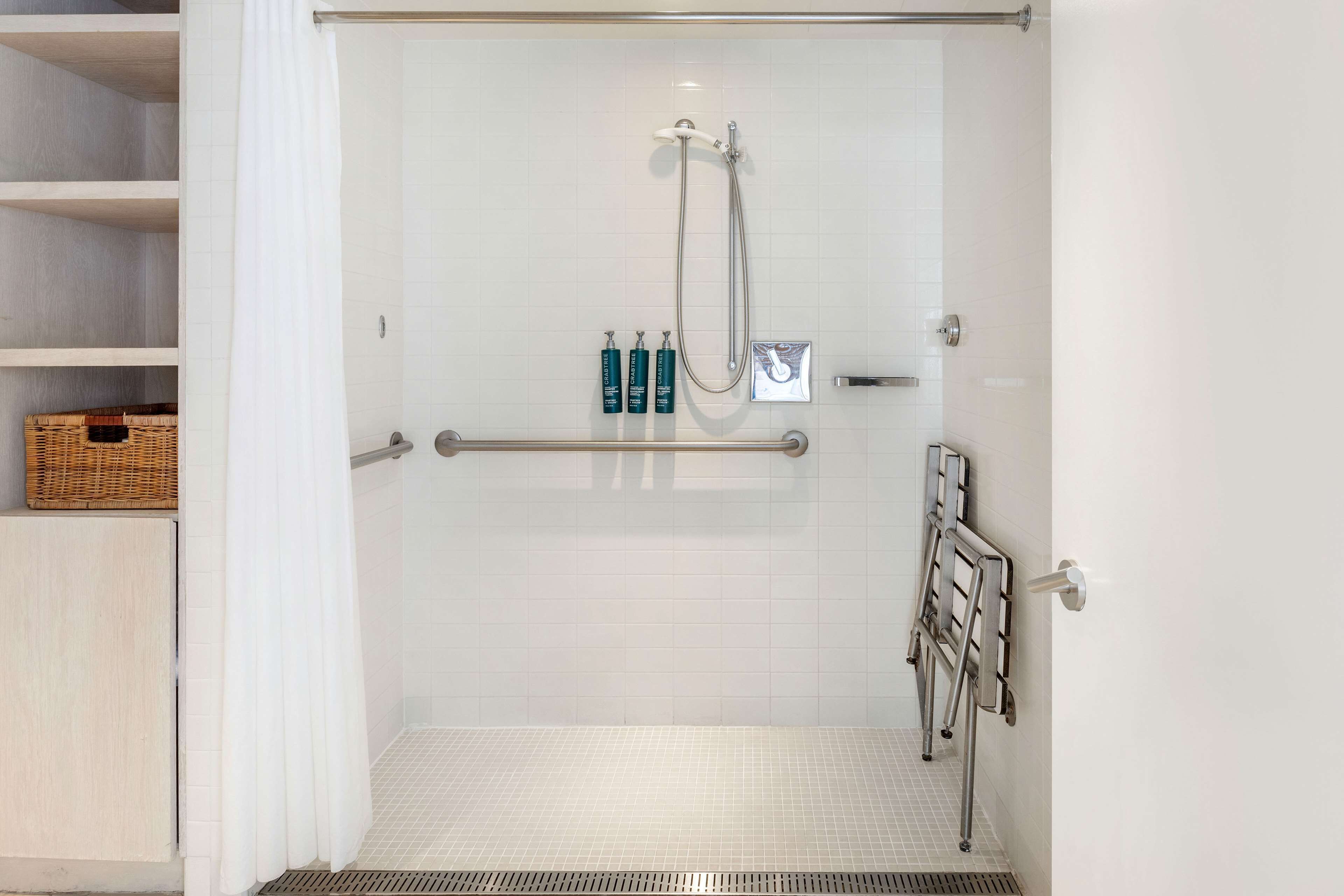 A shower area with a glass door, a handrail, and a shelf with toiletries.