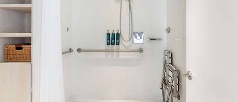 A shower area with a glass door, a handrail, and a shelf with toiletries.