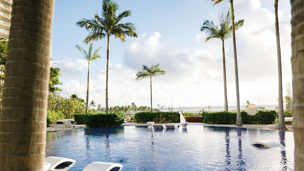 A swimming pool with lounge chairs, palm trees, and a view of the ocean. - Hilton Vacation Club The Modern Honolulu (Honolulu)