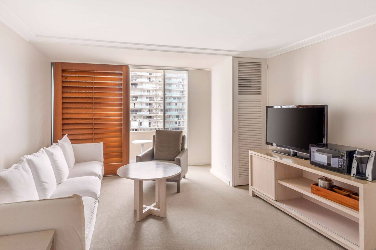A modern living room with a sofa, a round coffee table, a TV, and a microwave on a wooden cabinet.