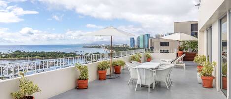 Un balcon avec une table et des chaises, des plantes en pot et une vue sur la mer et les bâtiments.