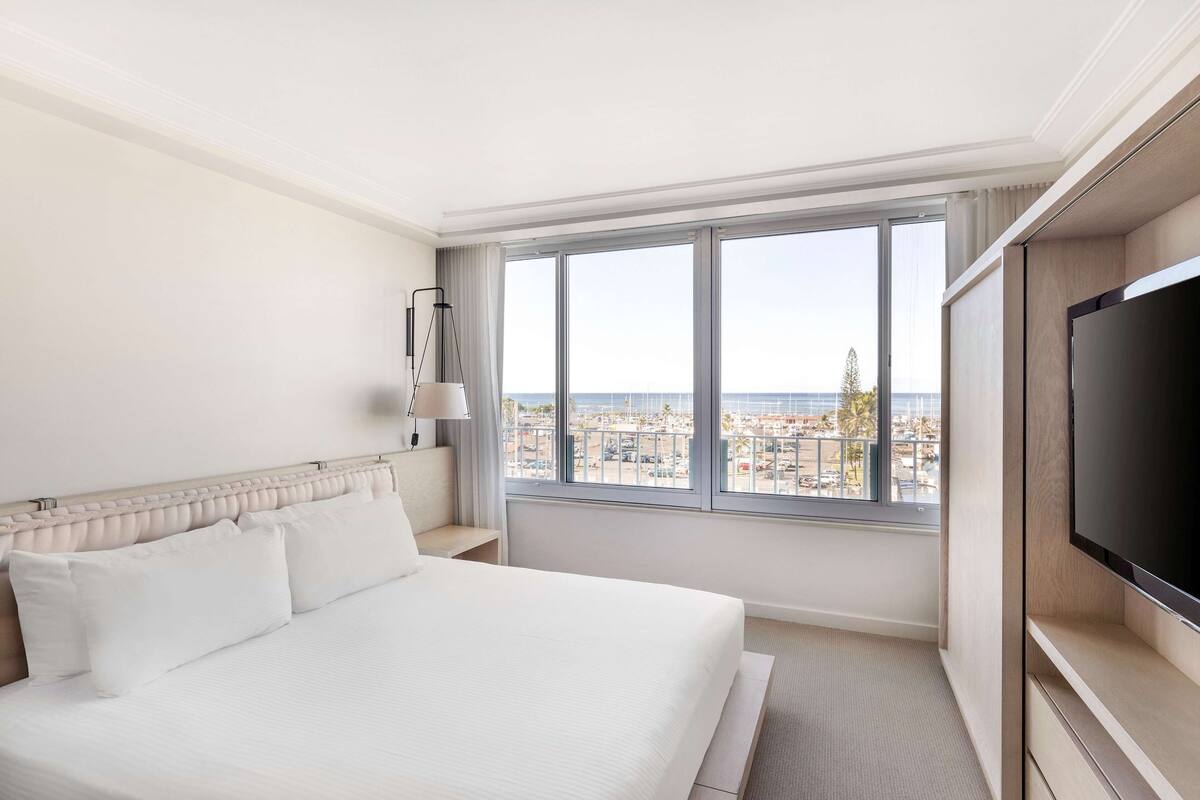 A hotel room with a large bed, a TV, and a window with a city view.