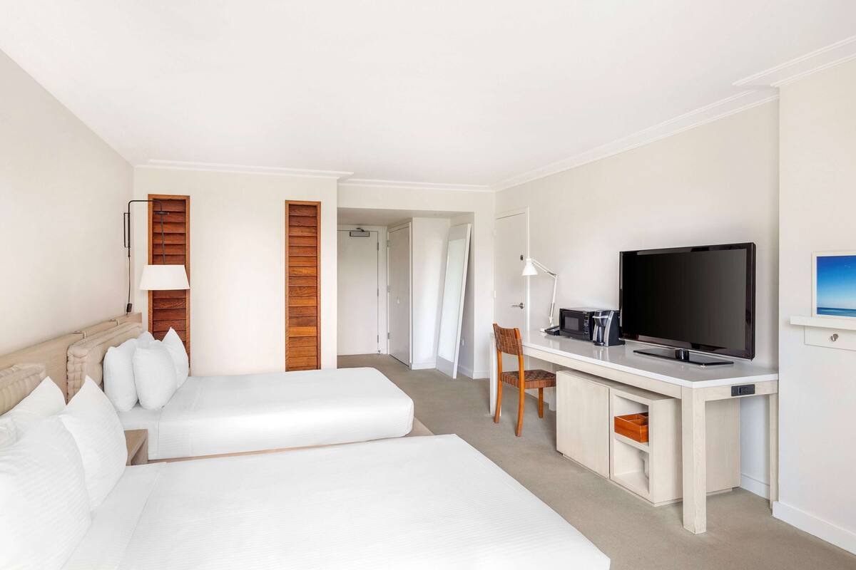 A hotel room with two beds, a desk with a TV, and a chair.