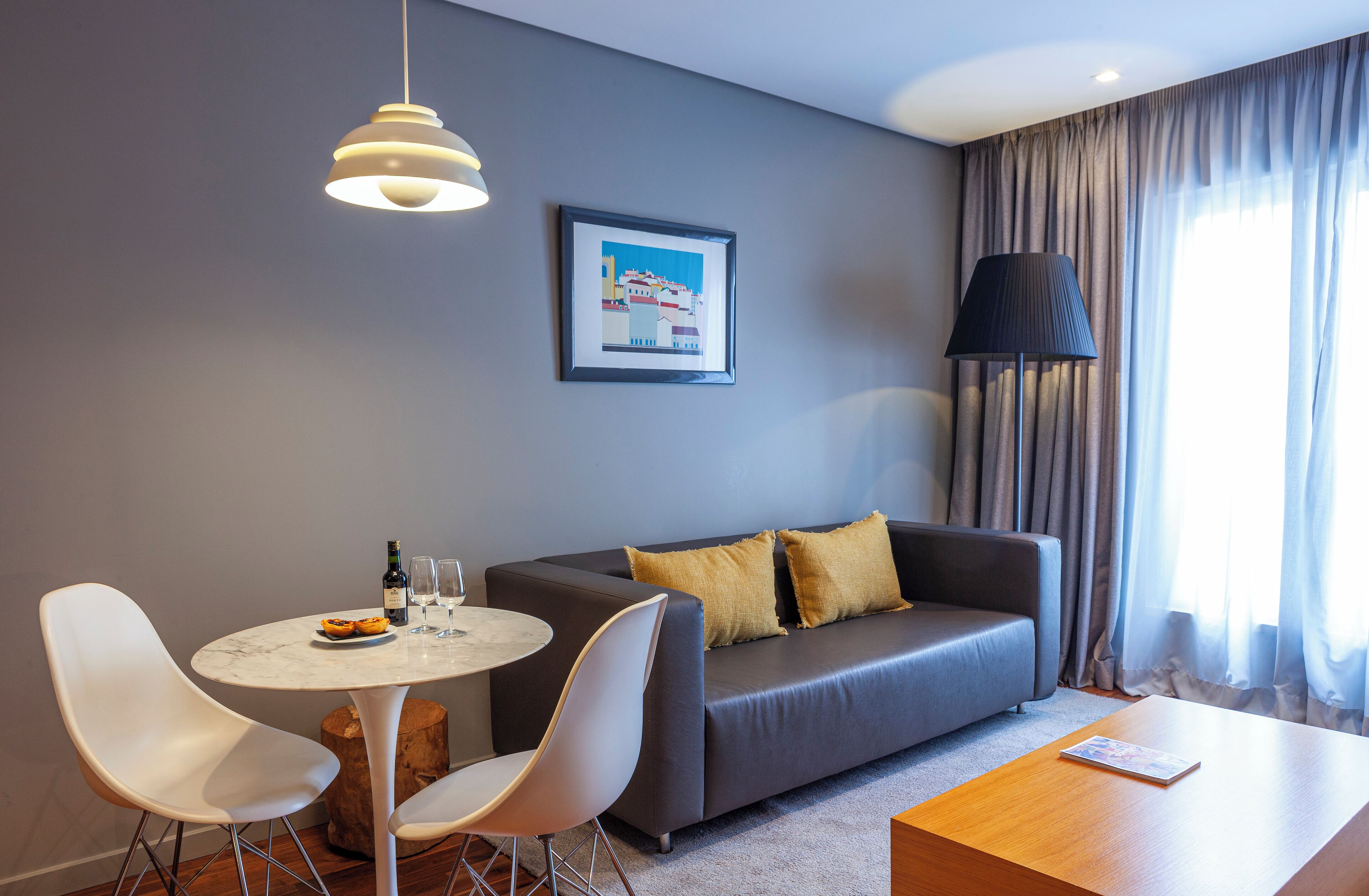 Ein modernes Wohnzimmer mit einem grauen Sofa, weißen Sesseln, einem runden Tisch und einem gerahmten Bild an der Wand.