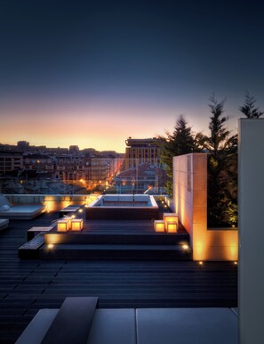 Eine Dachterrasse mit Sitzbereichen, einem Pool und Blick auf die Skyline der Stadt im Abendlicht.