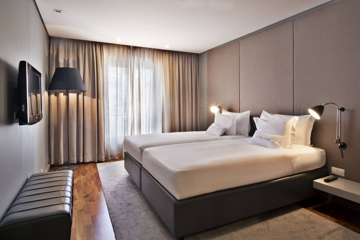 Ein modernes Hotelzimmer mit einem großen Bett, zwei Nachttischen, einem Flachbildfernseher und einem großen Fenster mit Vorhängen.
