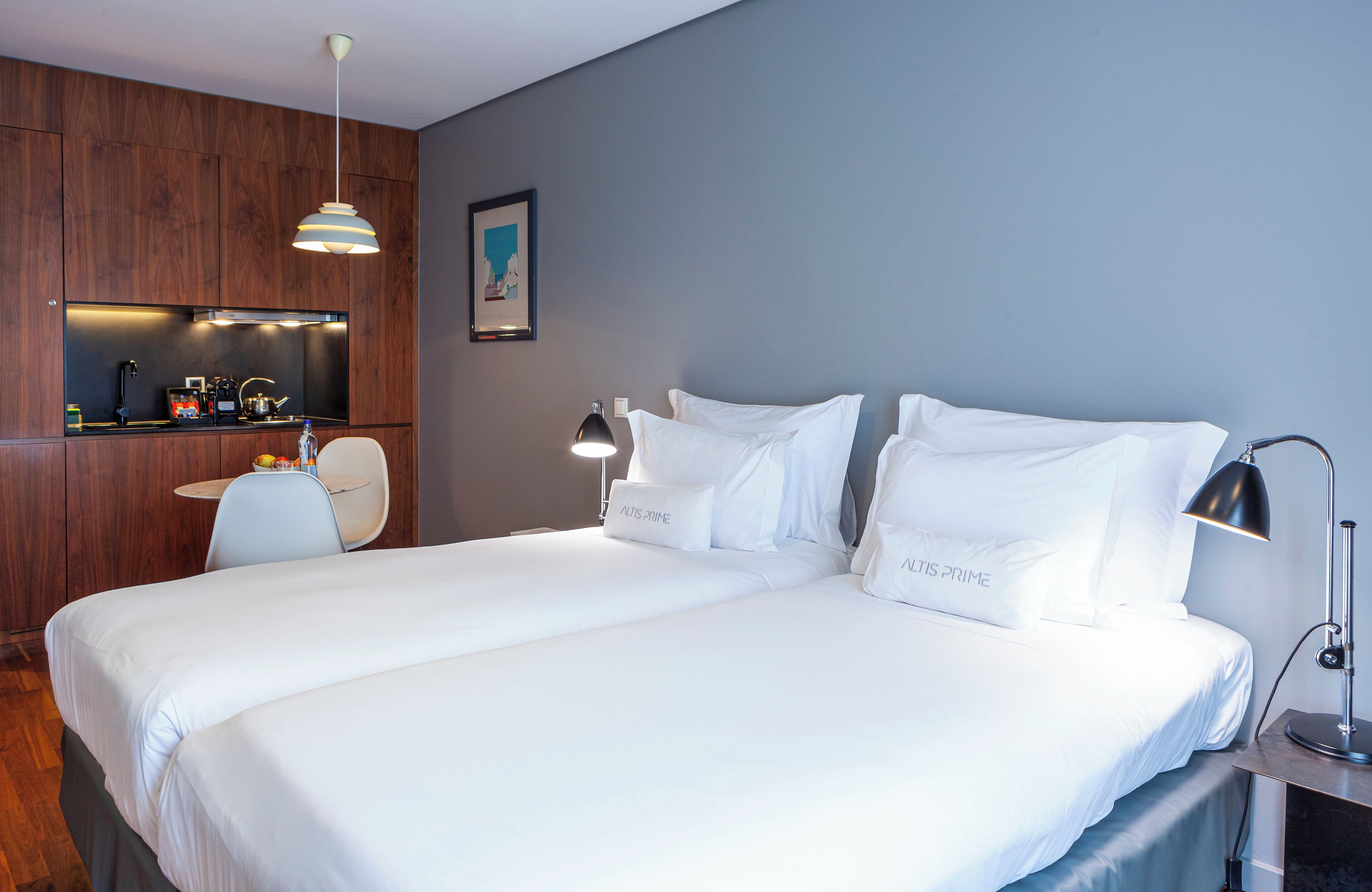A hotel room with a large bed, a desk with a chair, a coffee machine, and a wall-mounted shelf.
