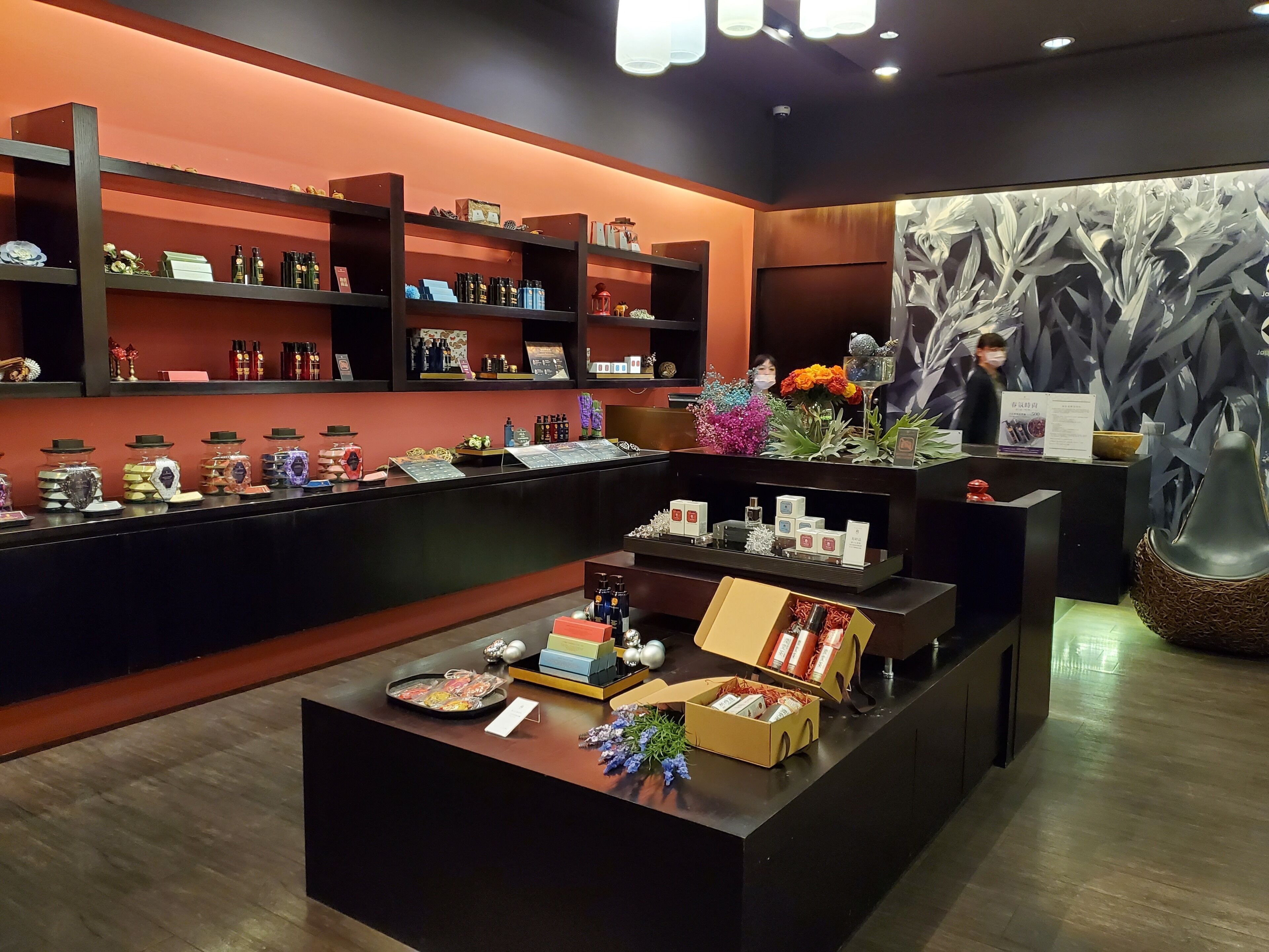 A well-organized retail space with shelves displaying various products, a central display table with items, and a decorative wall with a plant arrangement.