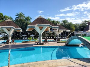 Zona de piscina con sillones de descanso, sombrillas y una piscina azul cristalina.