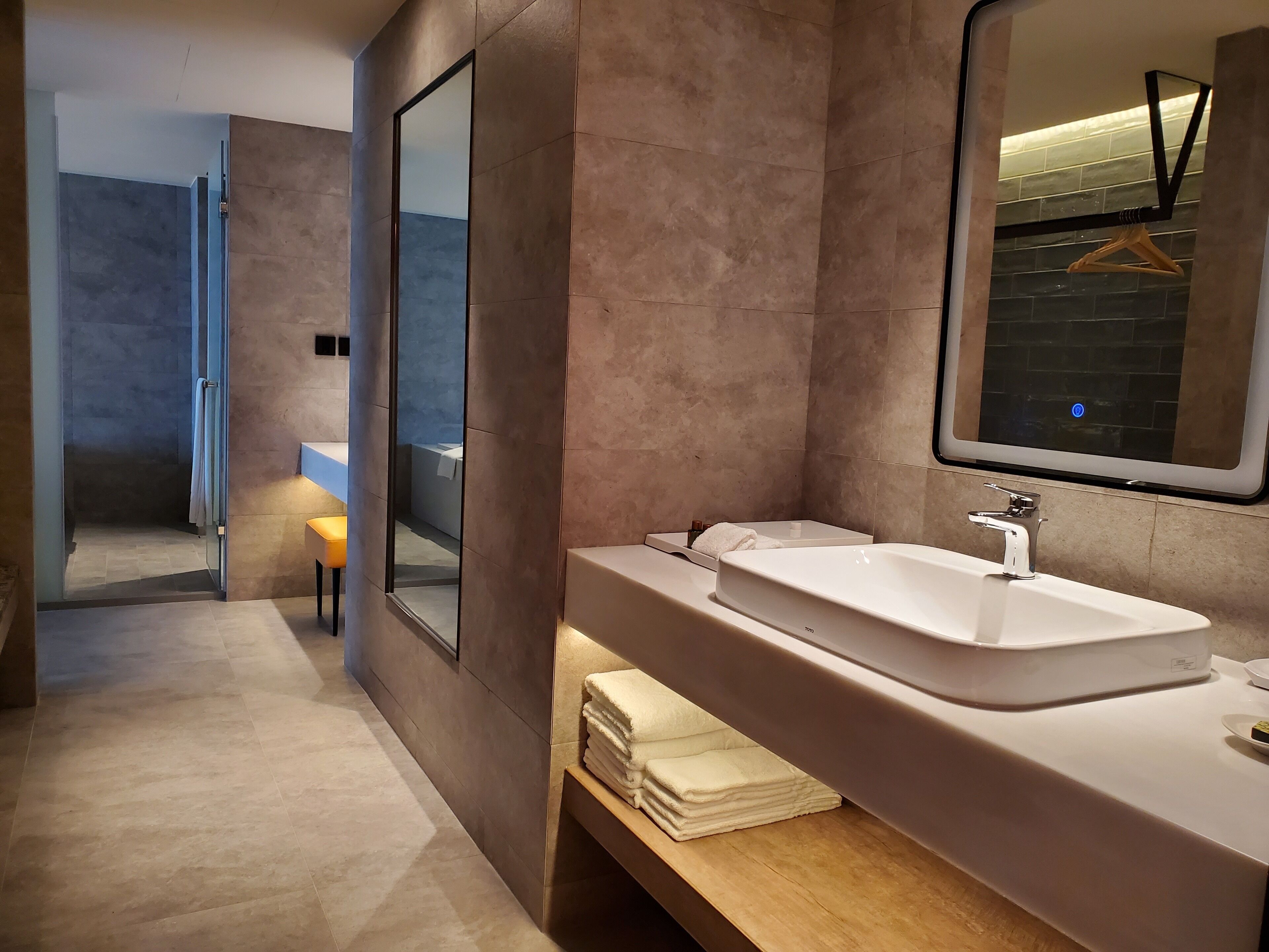 A modern bathroom with a large mirror, a white sink, and a wooden vanity.