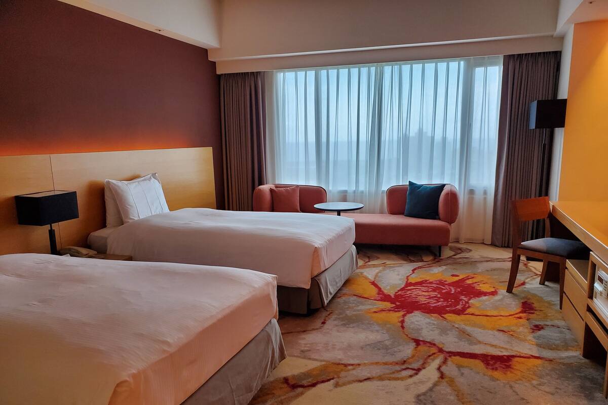 Een hotelkamer met twee bedden, een bank, een kleintje tafeltje en een stoel.