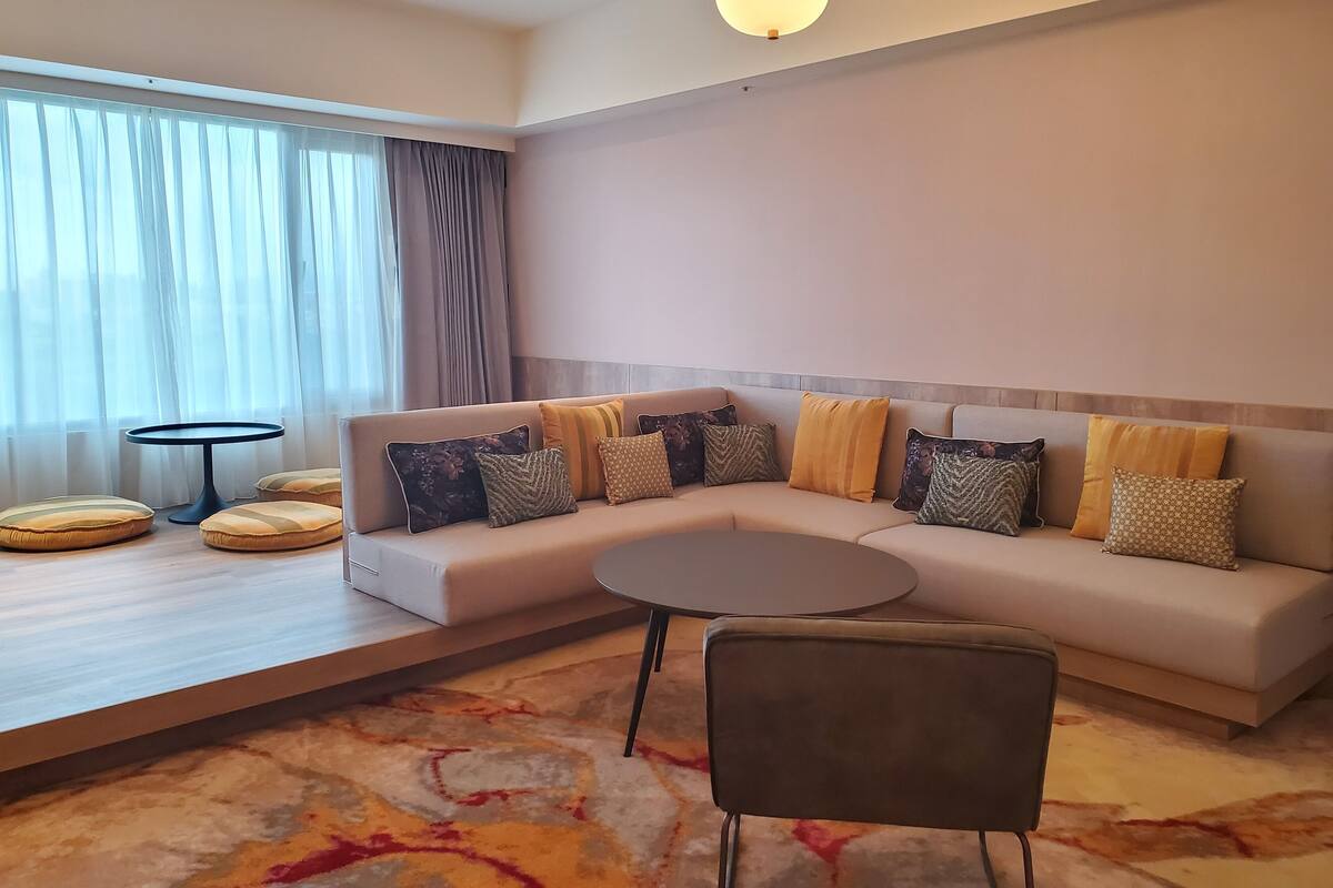 Een moderne woonkamer met een beige bank, een ronde salontafel en een kamerkleed met een patroon.