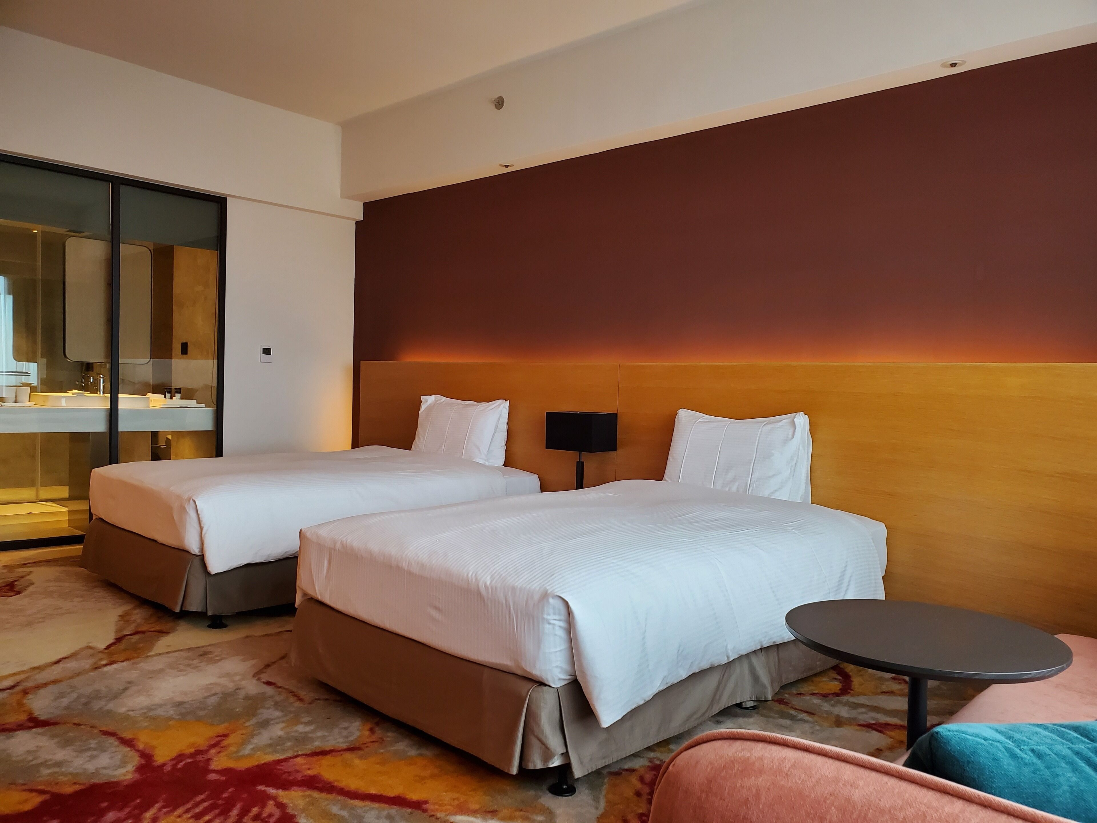 A hotel room with two beds, a small table, a sofa, and a large mirror.