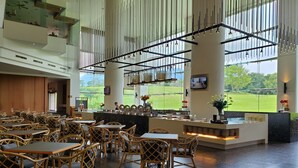 Un restaurant spacieux avec de hauts plafonds, de grandes fenêtres donnant sur un champ verdoyant, et un coin bar doté d’un comptoir et de tabourets.