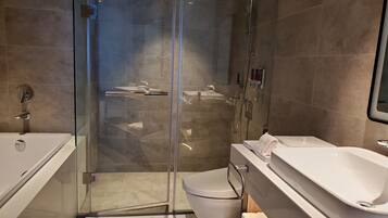 A modern bathroom with a glass-enclosed shower, a white bathtub, and a toilet.