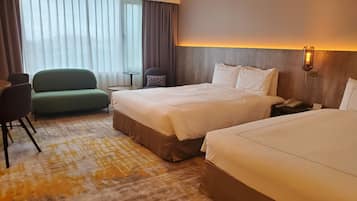 A hotel room with a large bed, a smaller bed, a sofa, a chair, a small table, and a bedside lamp.