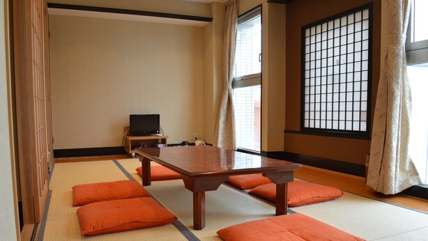 Une pièce de style japonais traditionnel, avec un sol recouvert de tatamis, une table basse et des coussins orange.