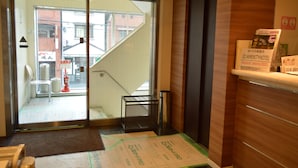 Un espace d’accueil d’hôtel avec une porte vitrée donnant sur un escalier, une petite table en métal et un extincteur.