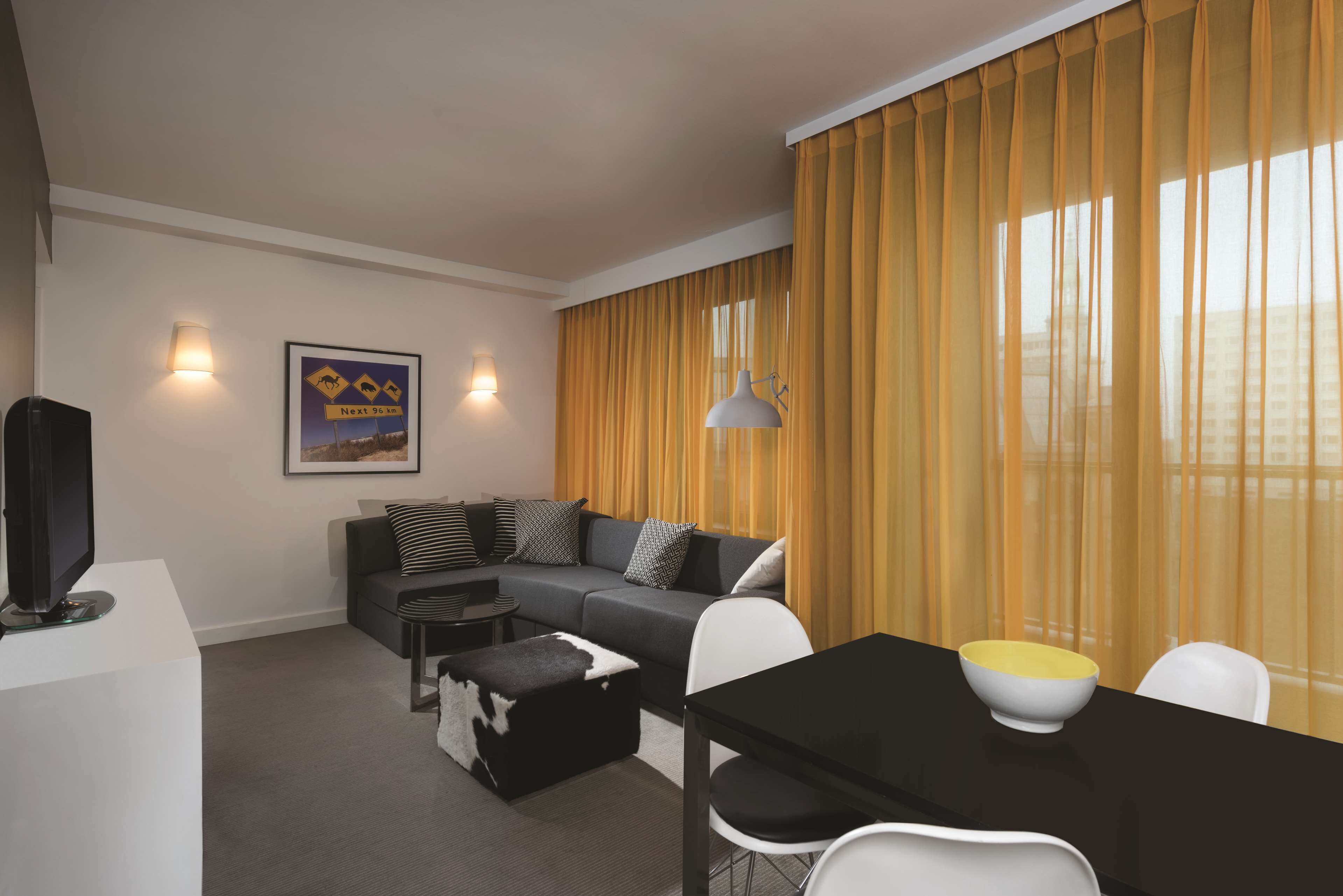 A modern living room with a sectional sofa, a dining table with chairs, a flat-screen TV on a white stand, and a framed picture on the wall.