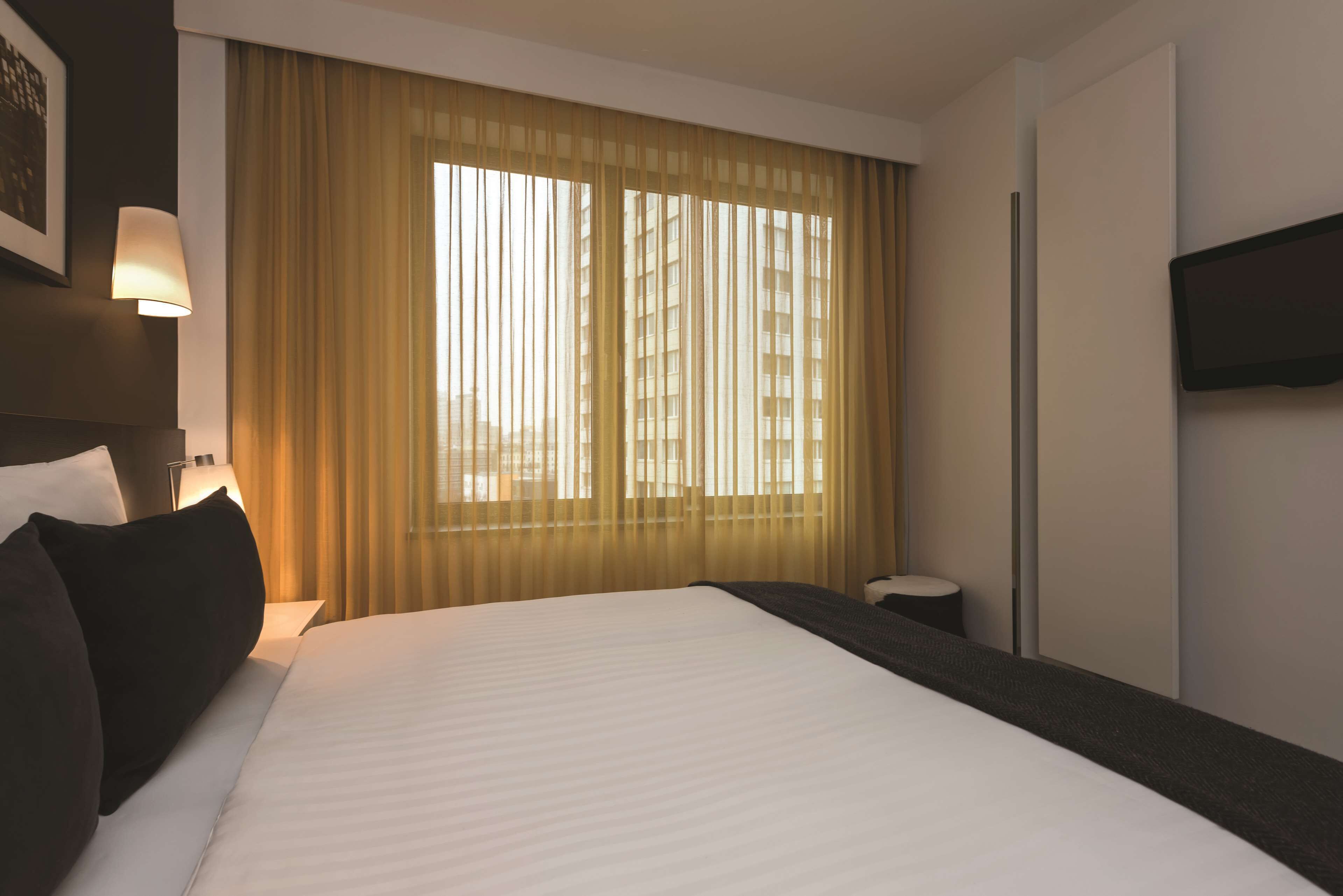 Une chambre d’hôtel avec un grand lit, une table de chevet, une lampe et une fenêtre avec des rideaux.