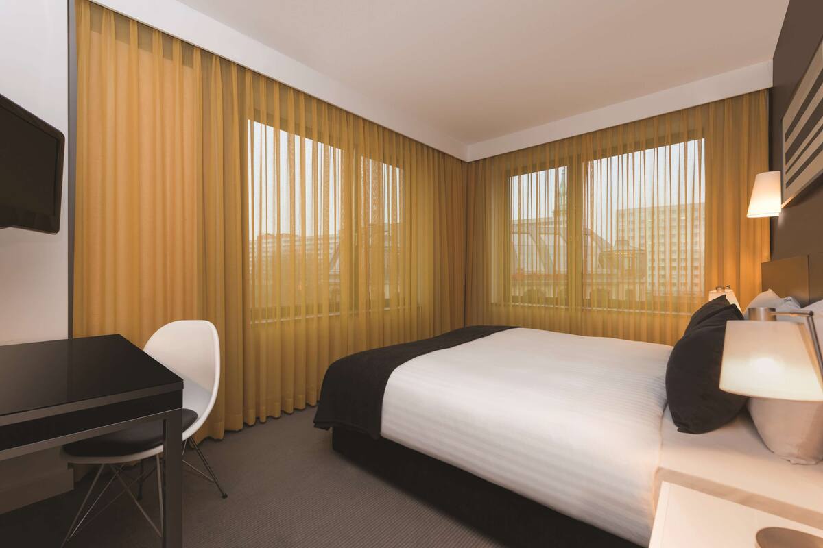 Una habitació d'hotel amb llit, escriptori, cadira i làmpada.
