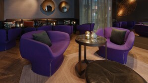 Ein moderner Lounge-Bereich mit violetten Sitzgelegenheiten, einem runden Tisch mit Kerzen und dekorativen Spiegeln an der Wand.