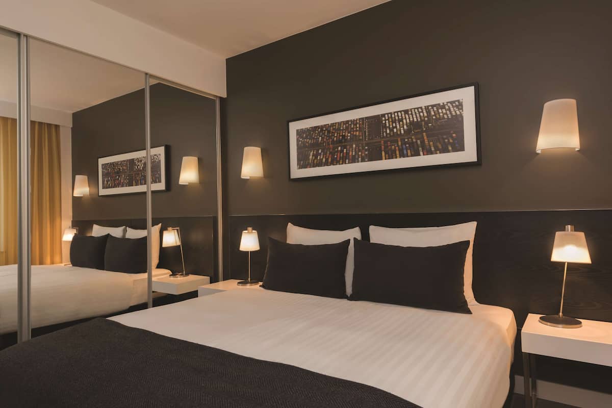 Habitació d'hotel amb un llit gran, dues taules de nit, un mirall i un quadre al mur.