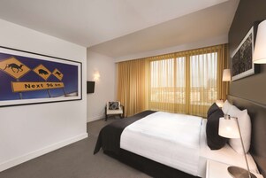 A hotel room with a large bed, a chair, a desk, and a window with curtains.
