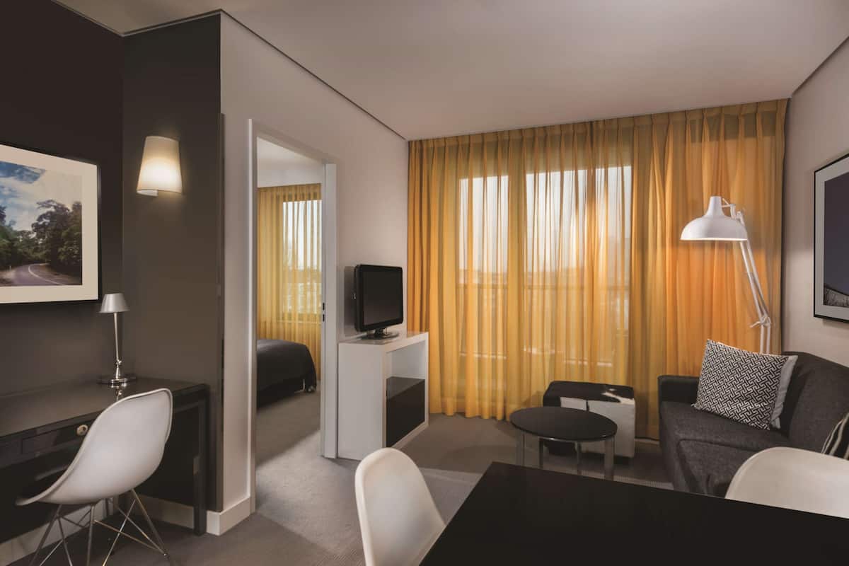Habitació d'hotel moderna amb escriptori, televisió, sofà i taula de dinar.