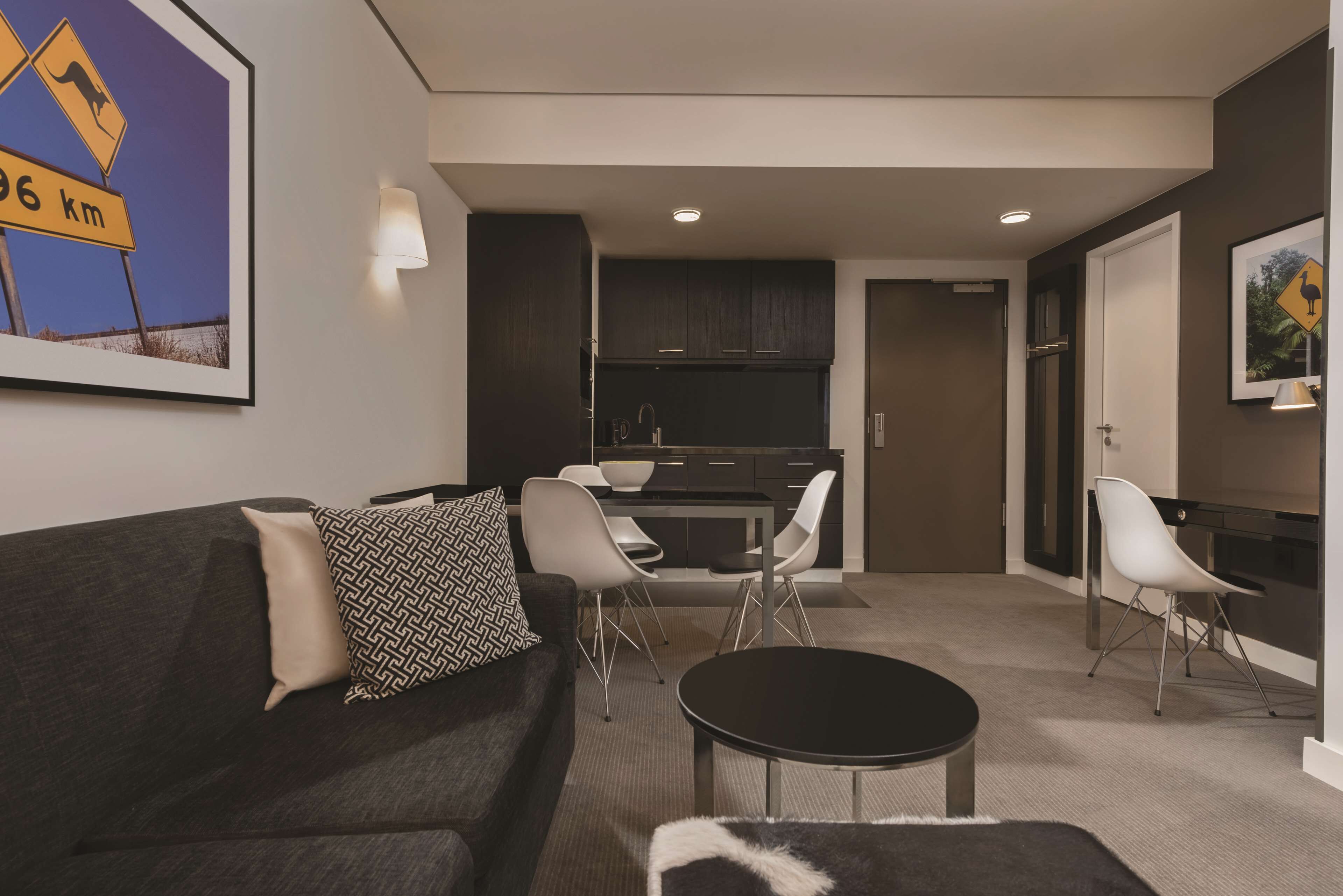 A modern living room with a dark grey sofa, a round coffee table, and a dining area with a kitchen in the background.