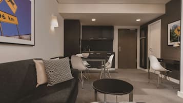 A modern living room with a dark grey sofa, a round coffee table, and a dining area with a kitchen in the background.