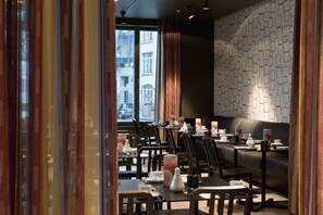 Un restaurant moderne avec des tables dressées pour le service, un mur décoré de motifs et de grandes fenêtres.
