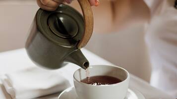 A hand pouring tea from a ceramic teapot into a white cup on a saucer.