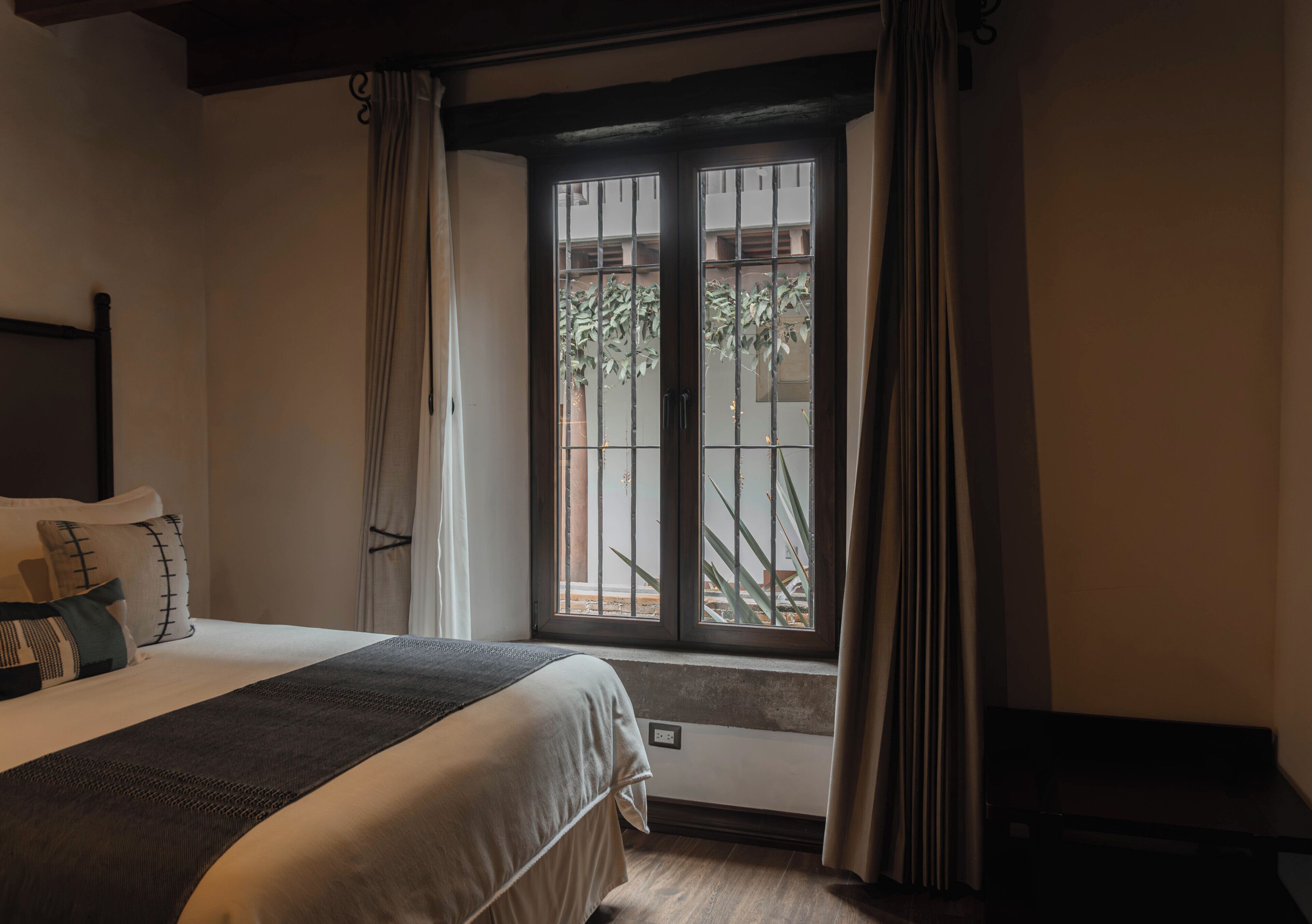Ein Hotelzimmer mit einem Bett, einem Fenster mit Vorhängen, Blick auf Grünfläche und einem kleinen Tisch.