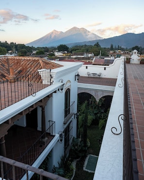 A rooftop terrace with a view of a mountain, terracotta roof tiles, and a white building with a balcony.