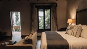 Une chambre à coucher avec un lit, une table de chevet, une lampe, une fenêtre avec des rideaux et une vue sur la verdure à l’extérieur.