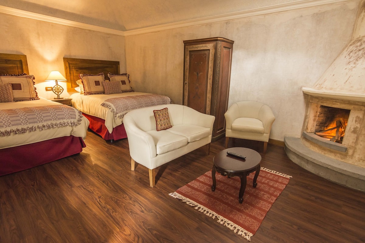 Ein Zimmer mit zwei Betten, einem weißen Sofa, einem Sessel, einem kleinen Tisch und einem Kamin.