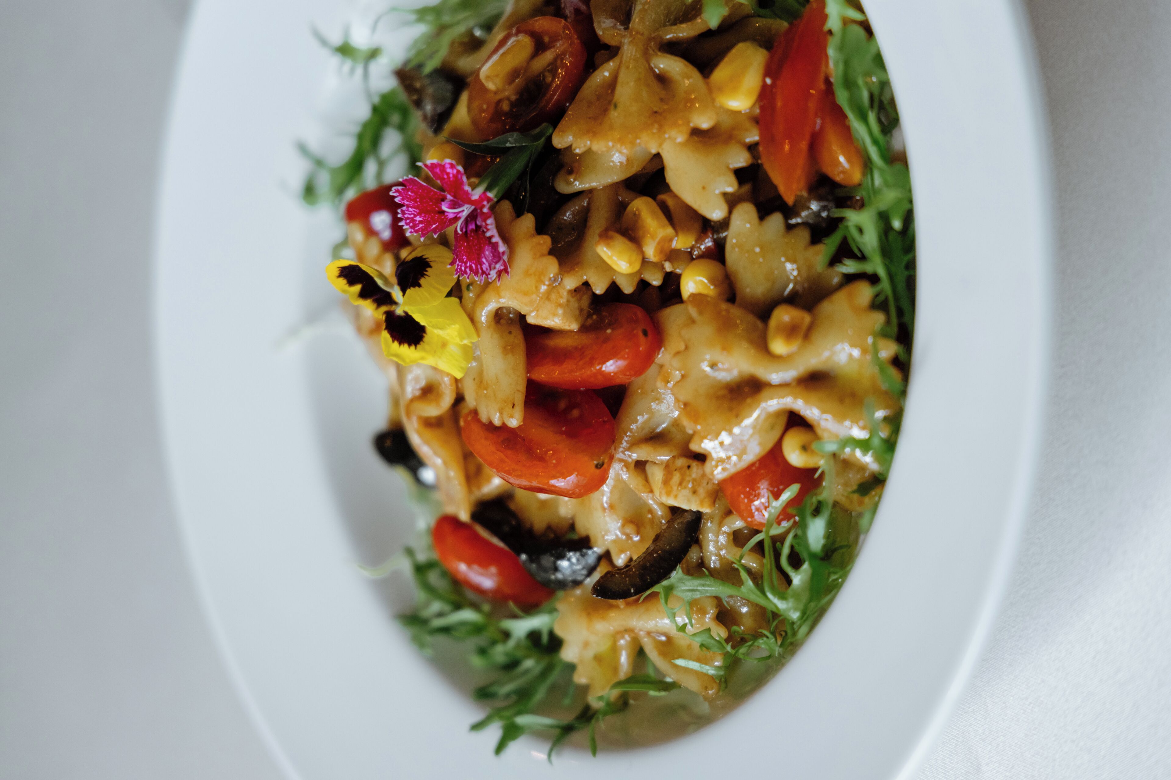 A close-up of a pasta dish with vegetables and a decorative flower on a white plate.