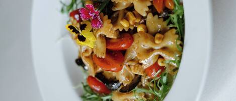 A close-up of a pasta dish with vegetables and a decorative flower on a white plate.