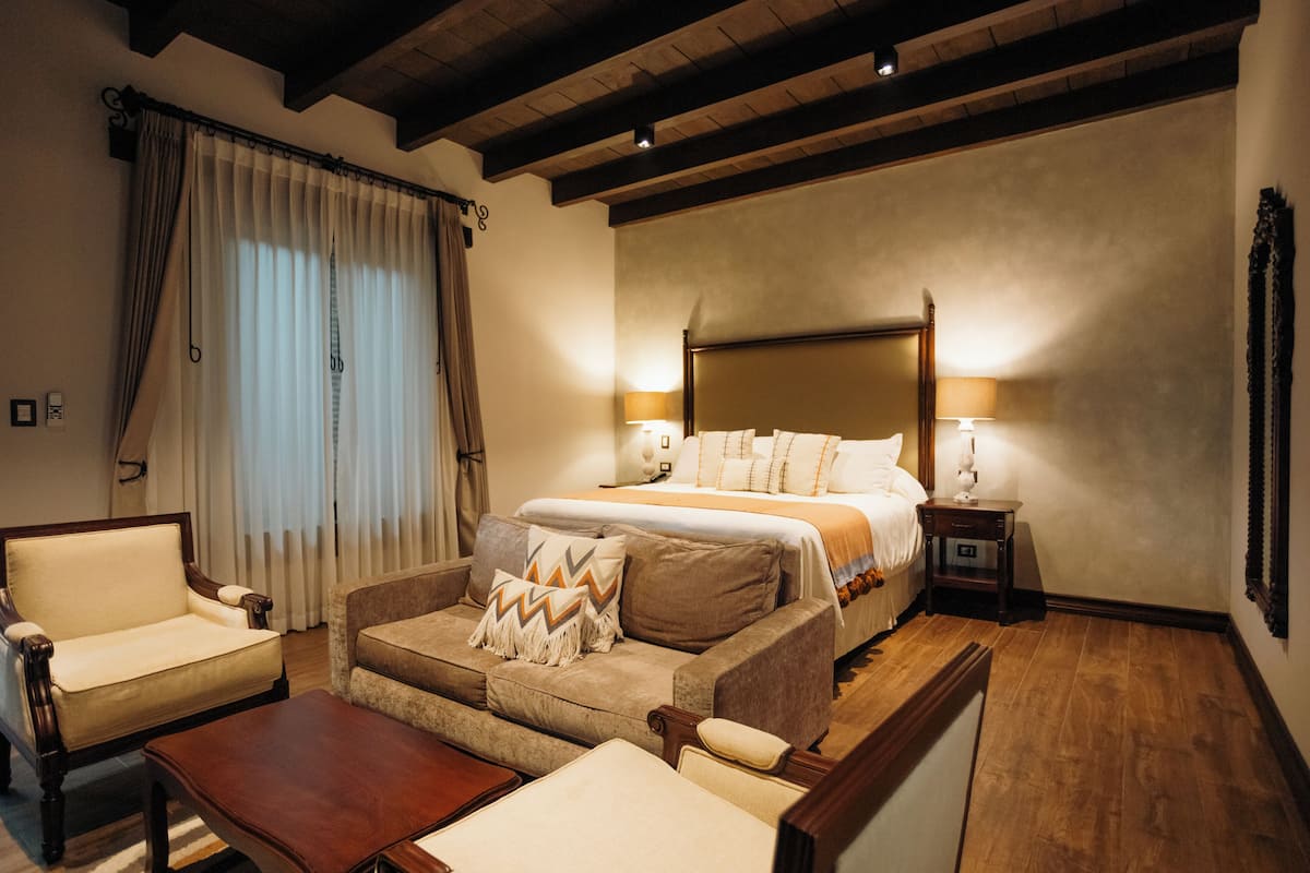 Ein Hotelzimmer mit einem großen Bett, zwei Nachttischen mit Lampen, einem Sofa, einem Sessel und Holzboden.