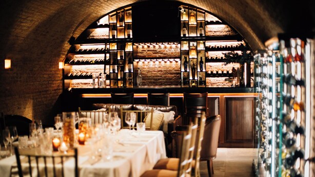 Un restaurant avec un mur en briques, des étagères à vin et des tables dressées pour le dîner.