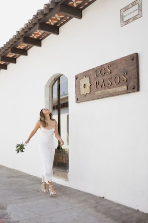 A person in a white dress standing in front of a sign that reads "LOS PASOS".