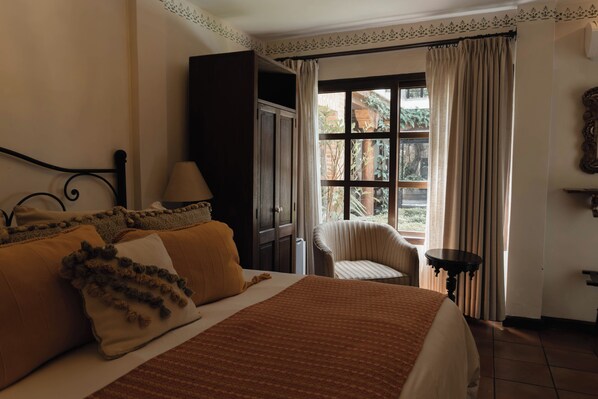 Un dormitorio con cama, una silla, una mesa y un ventanal con cortinas.